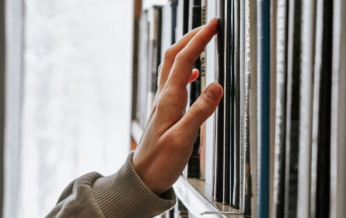 Hand touching books on library shelf